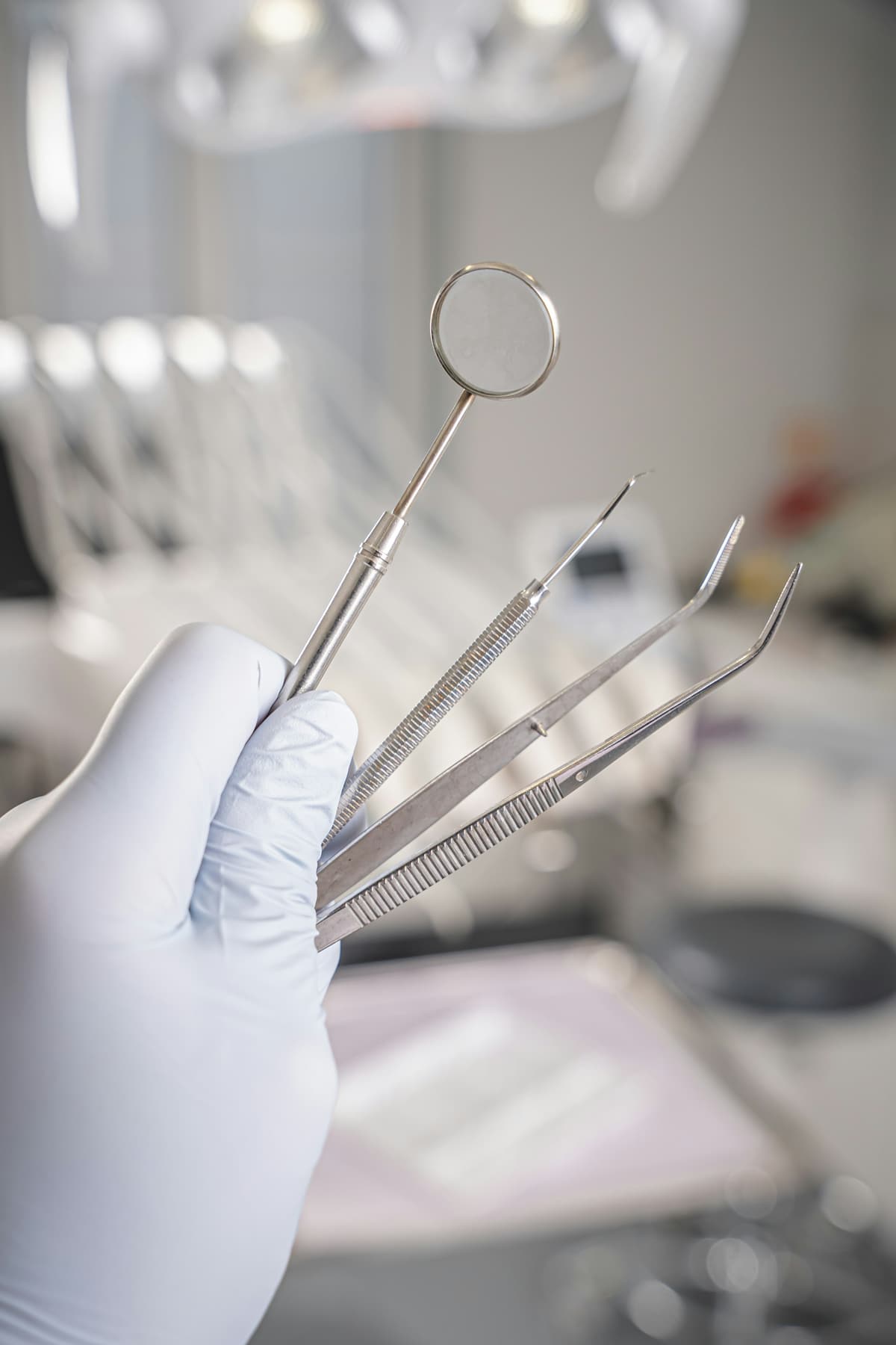 A gloved hand holding a dental mirror, probe and tweezers