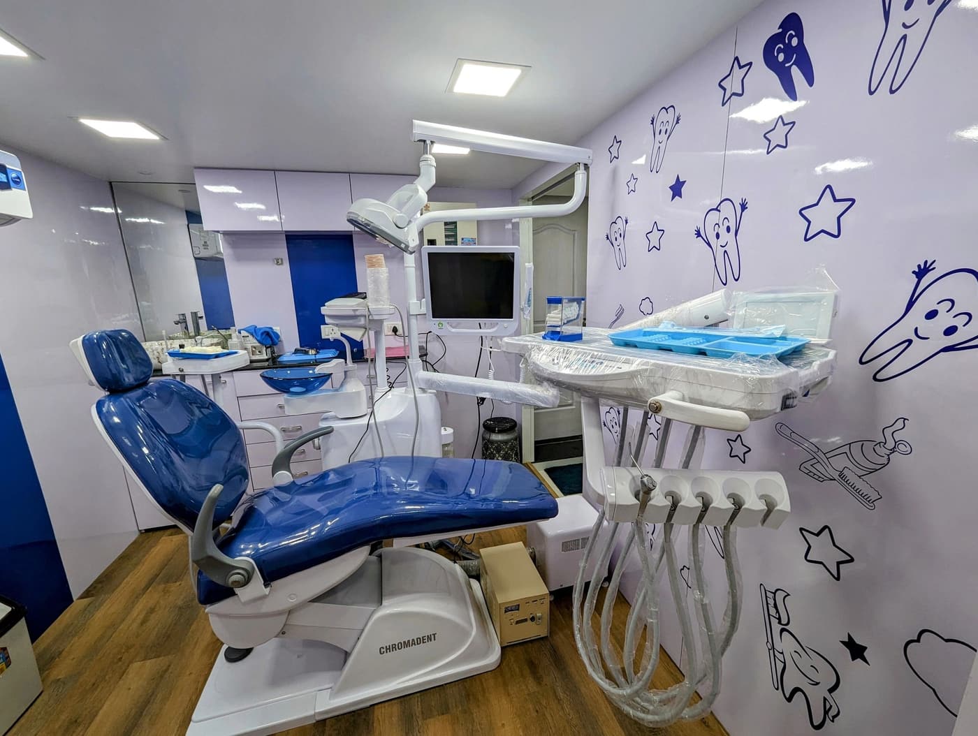 A treatment room at Suryaini Dental Clinic, with a blue dental chair and tooth drawings on the wall